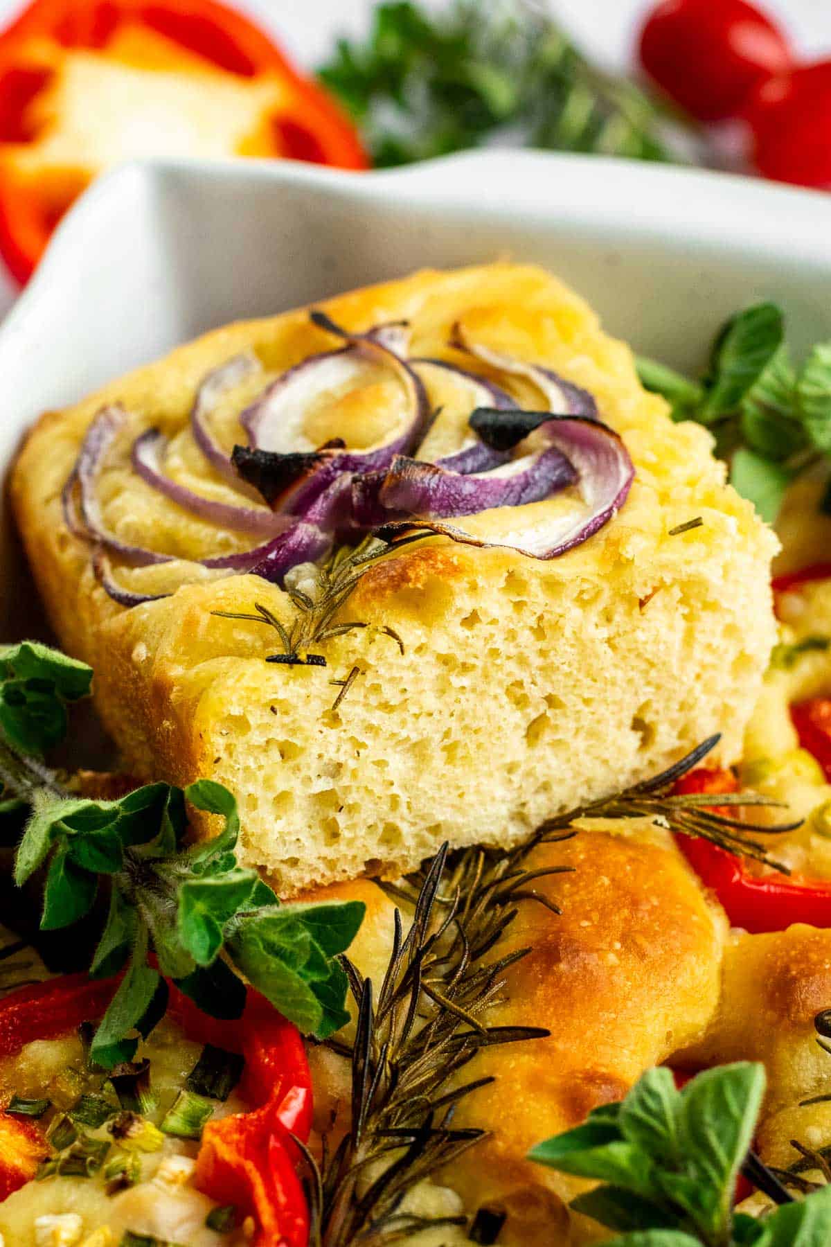 A large square of fluffy focaccia bread decorated with roasted red onion in the shape of a flower.