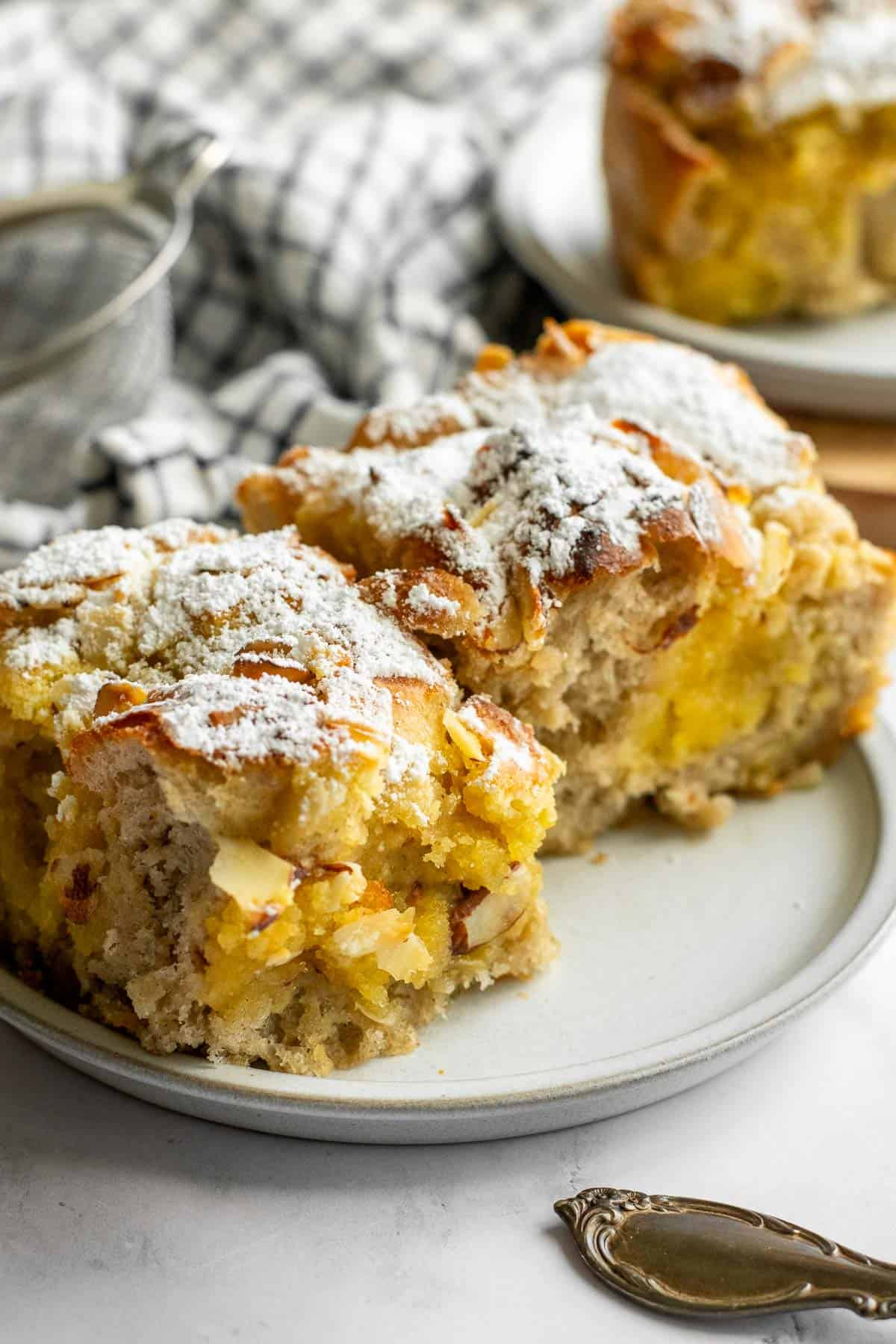 Two large pieces of focaccia filled with frangipane and topped with almonds and powdered sugar on a small grey plate. 