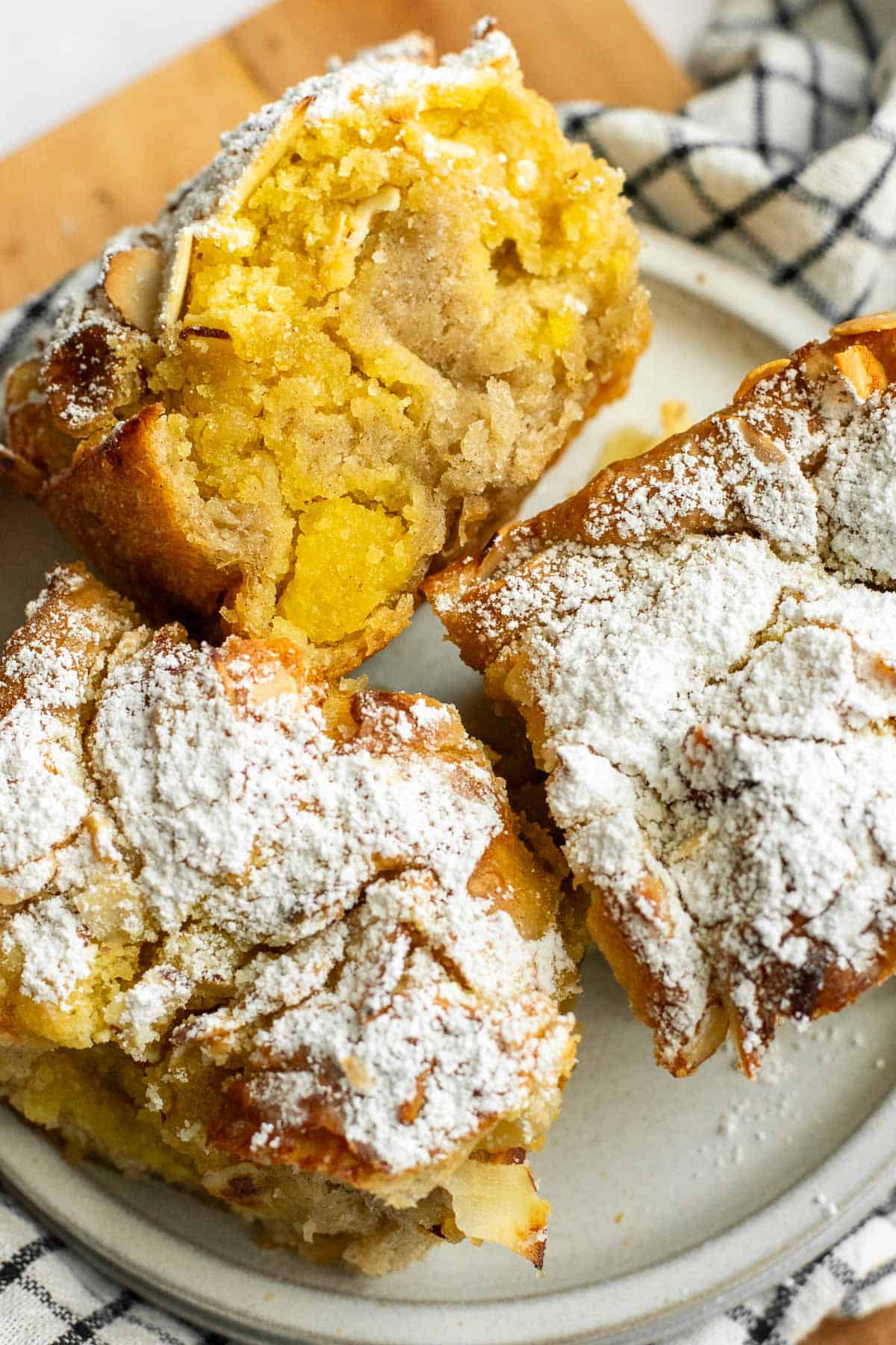 Three large squares of almond croissant focaccia on a small grey plate sitting on a black and white linen on a light wooden board.