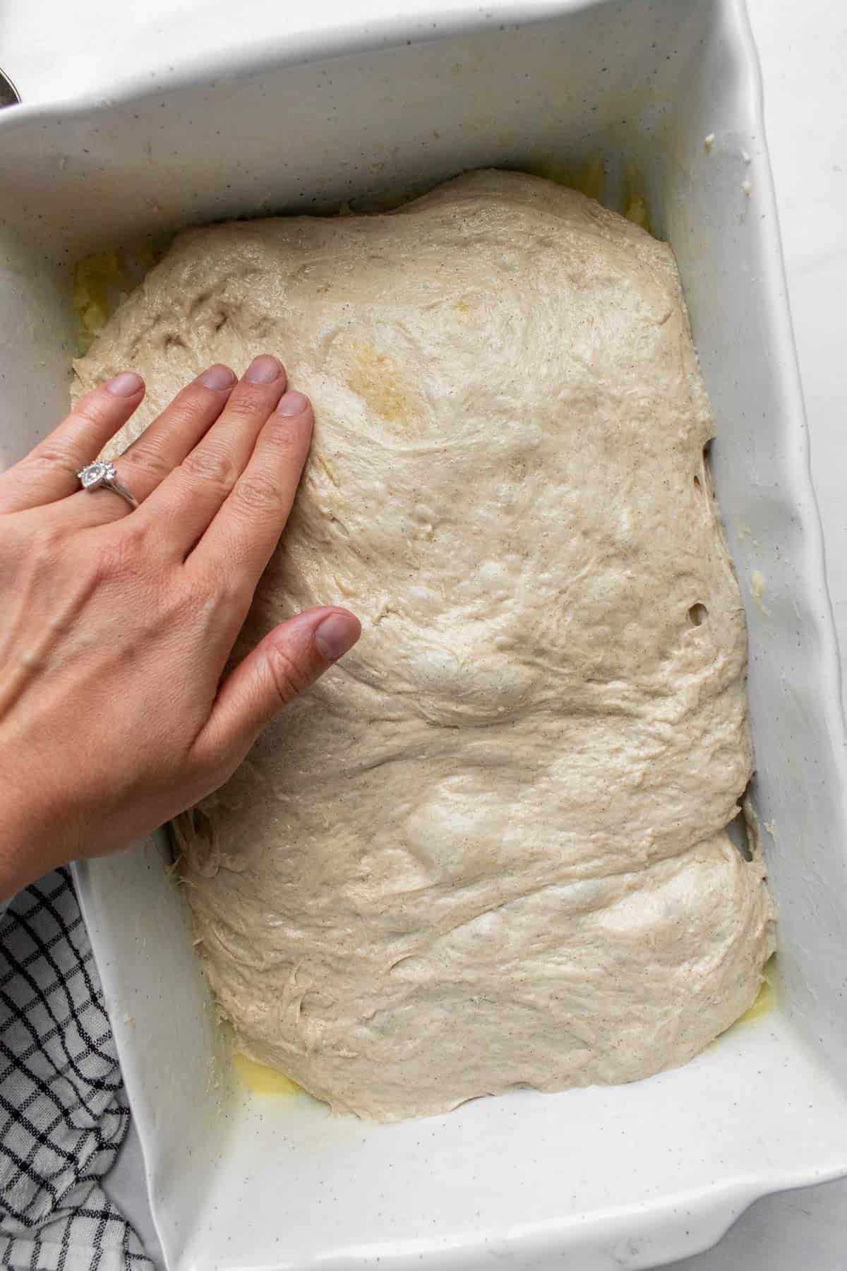 A hand pressing focaccia dough to fill a large baking dish.