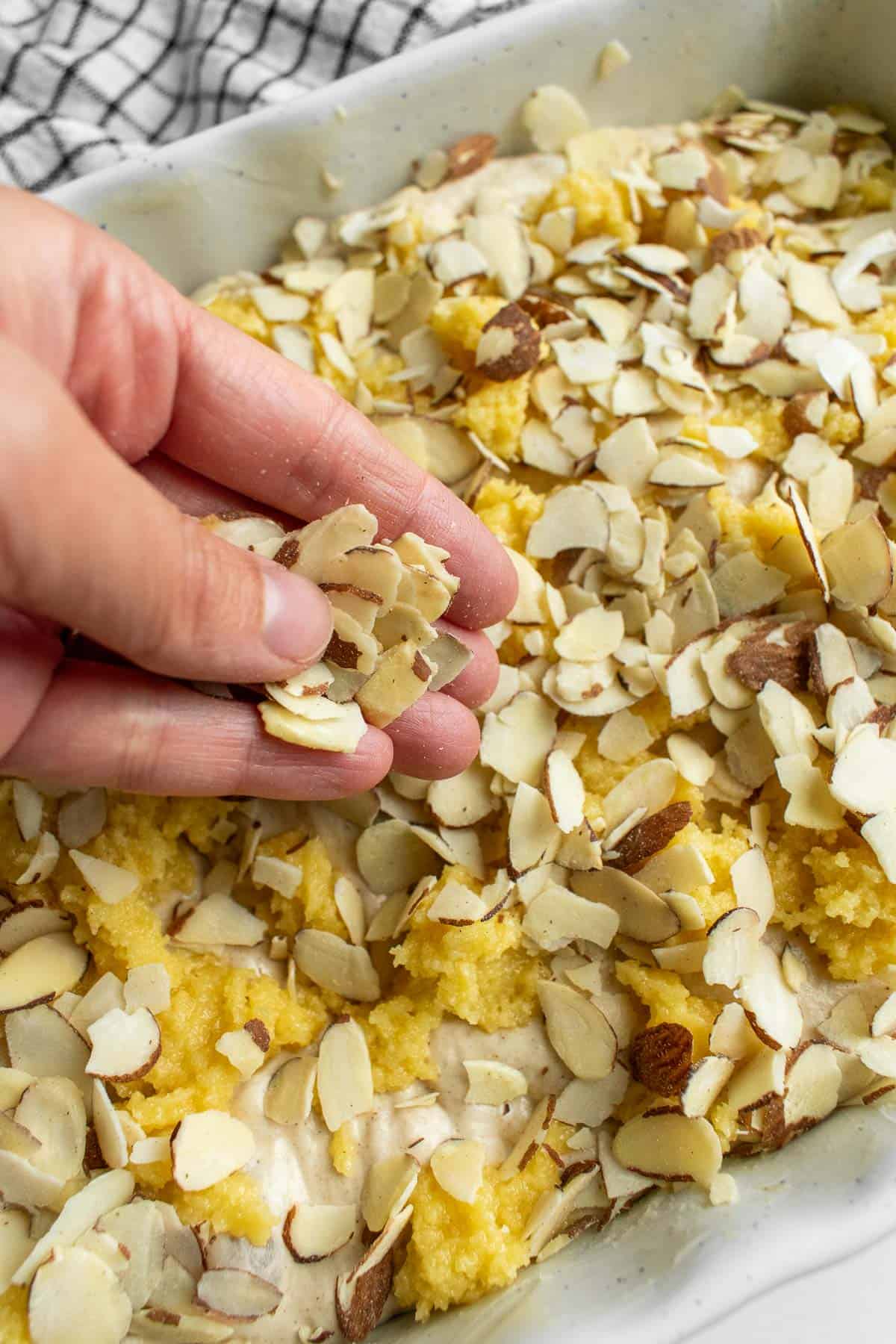 A hand sprinkling sliced almonds onto bread dough in a baking dish.