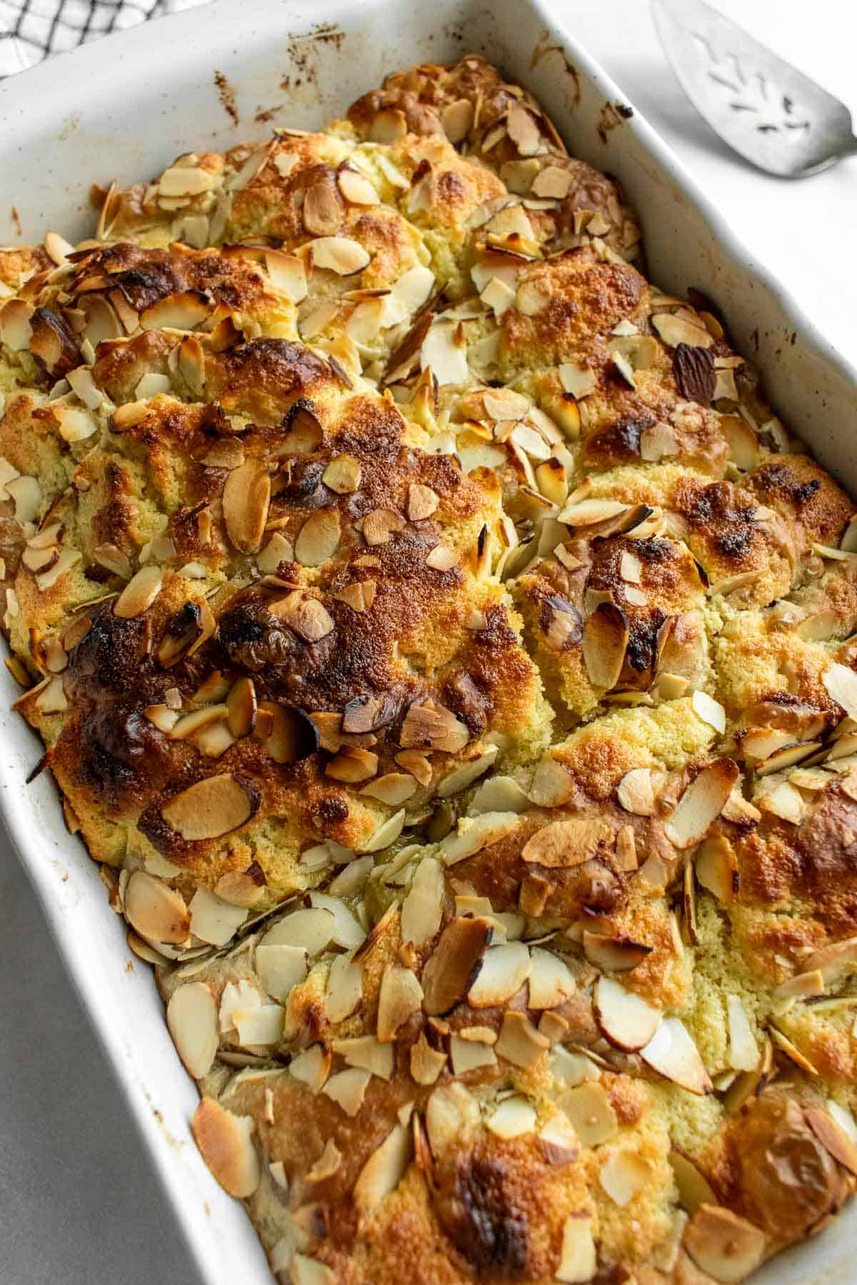 Golden baked focaccia bread in a white baking dish topped with frangipane and sliced almonds.
