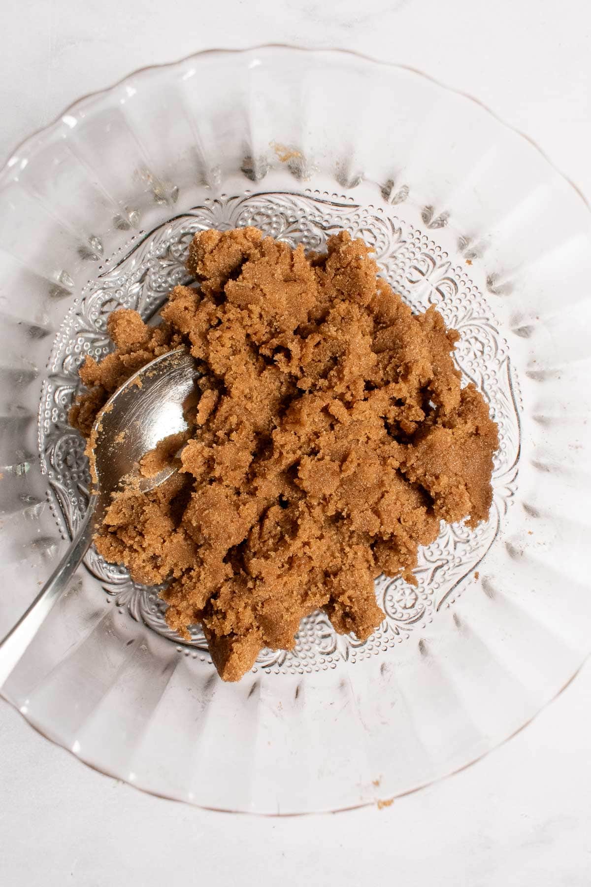A thick brown sugar mixture in a glass bowl with a metal spoon.