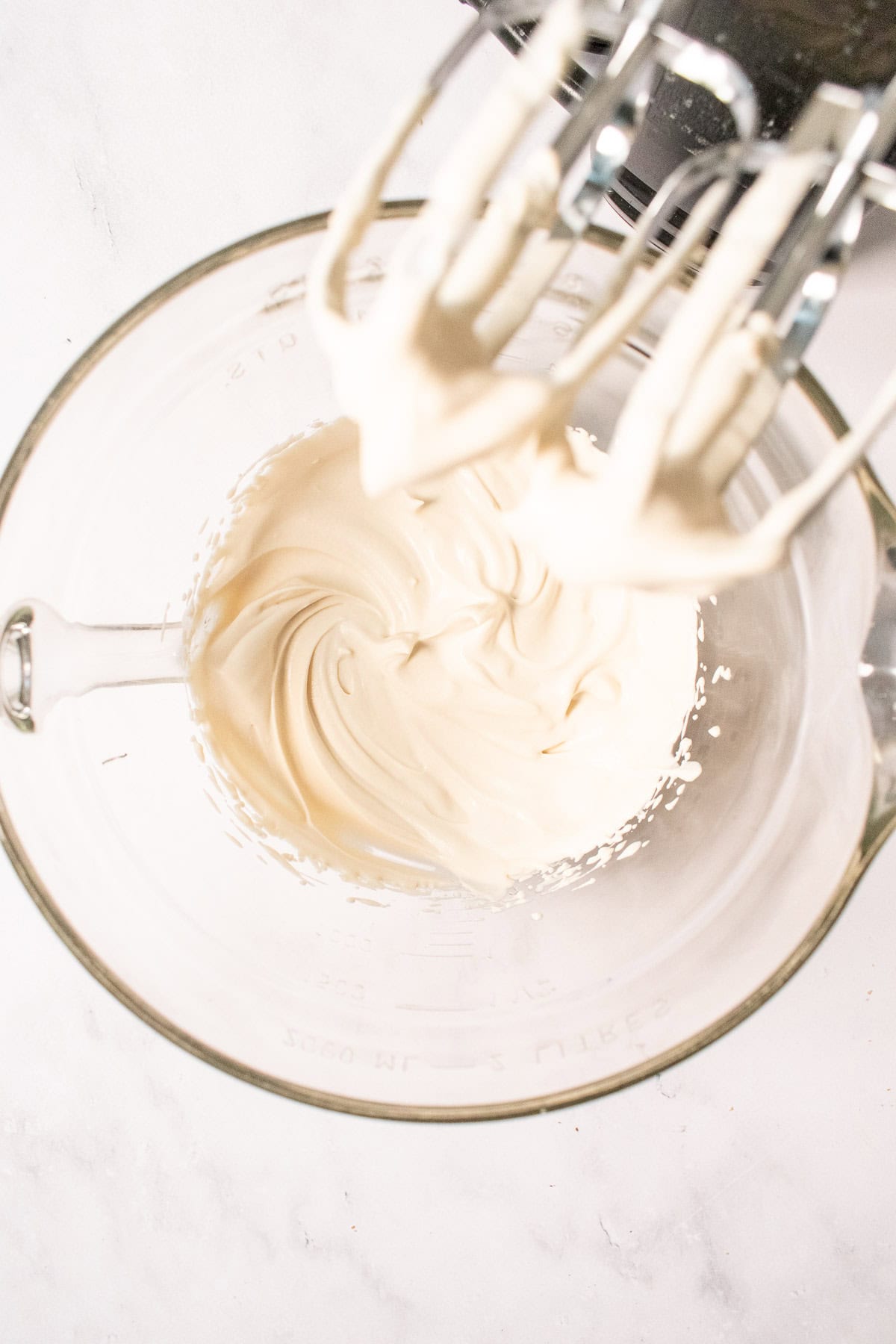 Whipped creme fraiche and heavy cream in a glass mixing bowl next to a hand mixer.