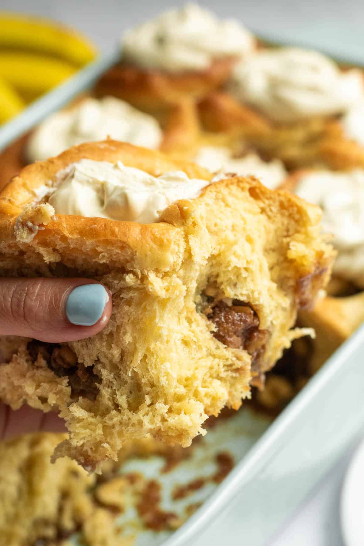 A hand holding a large, fluffy cinnamon roll with a nut filling and whipped cream on top.
