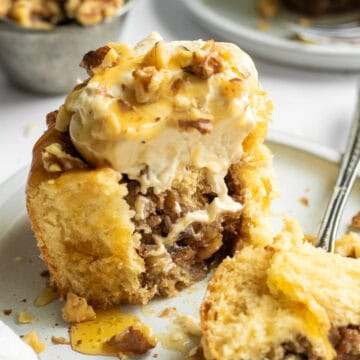 A large cinnamon roll filled with walnuts and mashed bananas with whipped cream and more walnuts on top, with a large piece cut off resting on a fork.