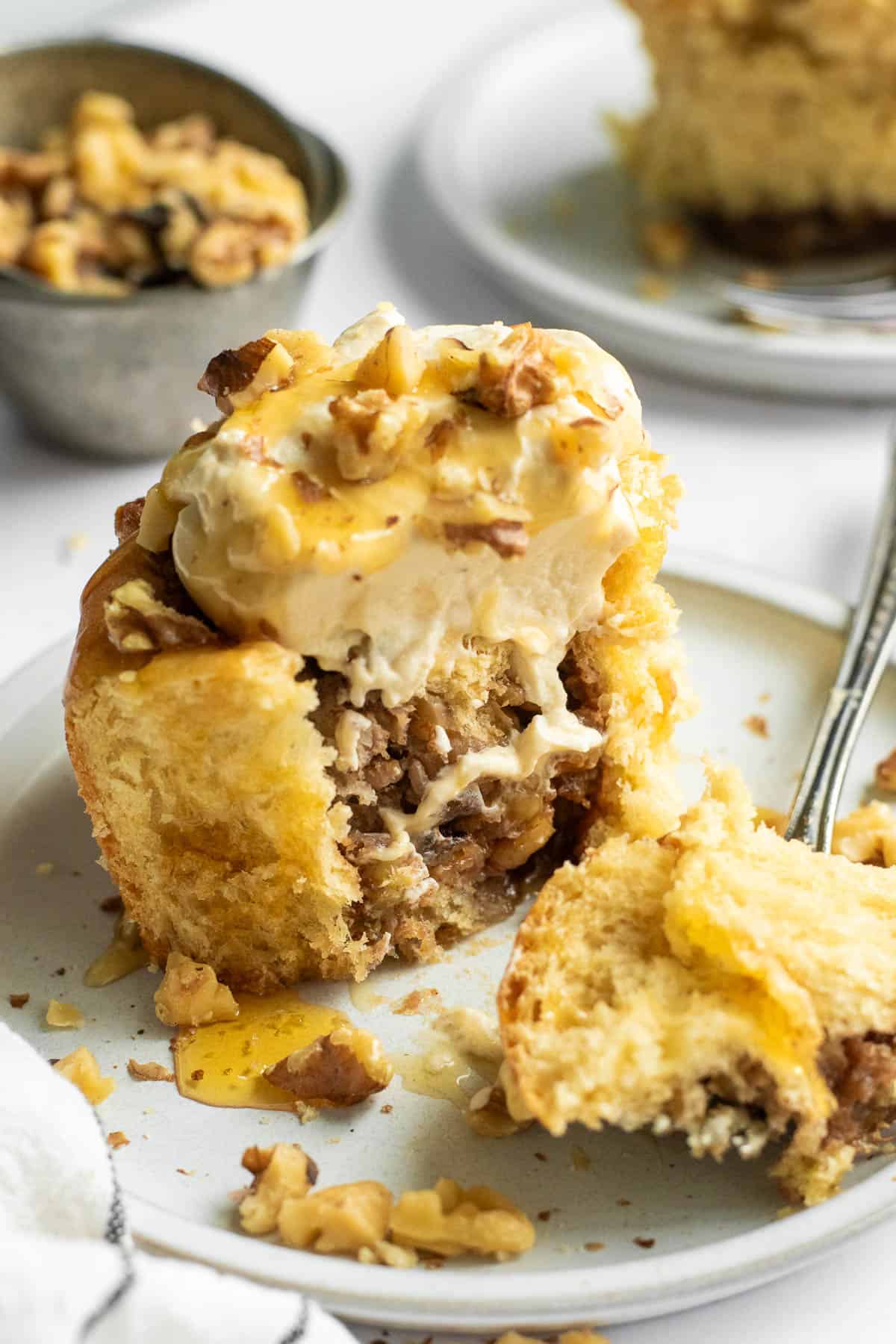 A large cinnamon roll filled with walnuts and mashed bananas with whipped cream and more walnuts on top, with a large piece cut off resting on a fork. 