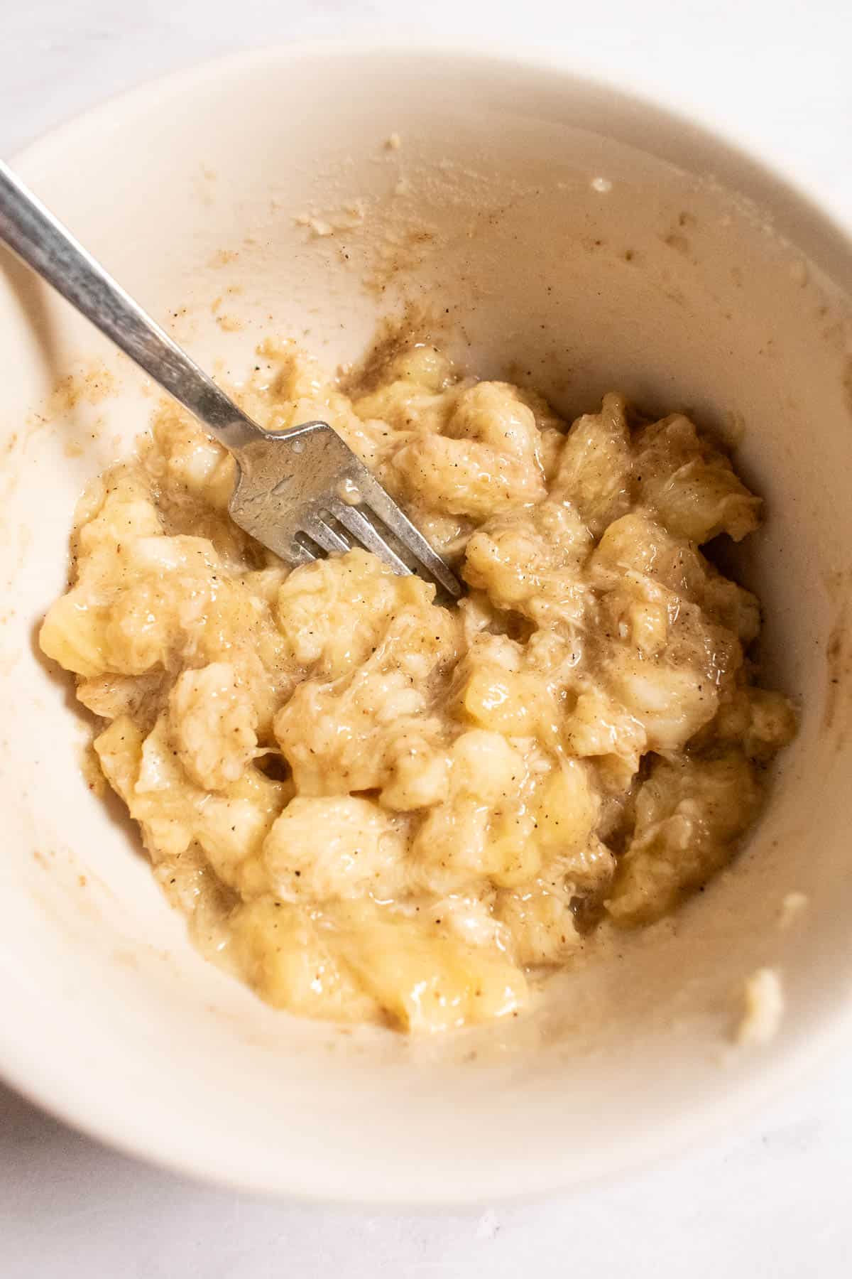 Mashed bananas in a beige bowl with a metal fork.