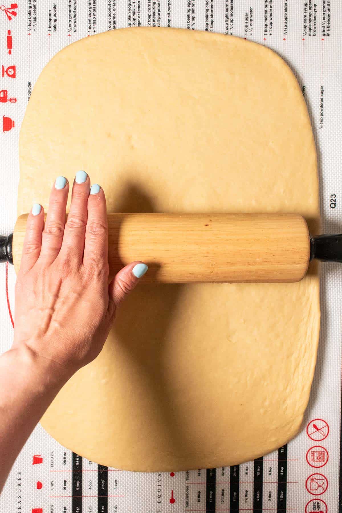 A hand rolling out enriched bread dough with a wooden rolling pin.