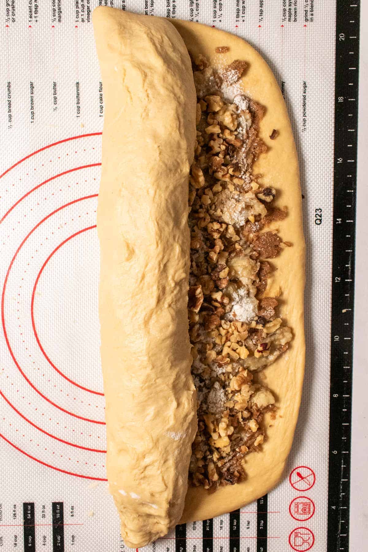 Cinnamon roll dough being rolled into a log, filled with cinnamon, brown sugar, butter, mashed bananas, and walnuts.