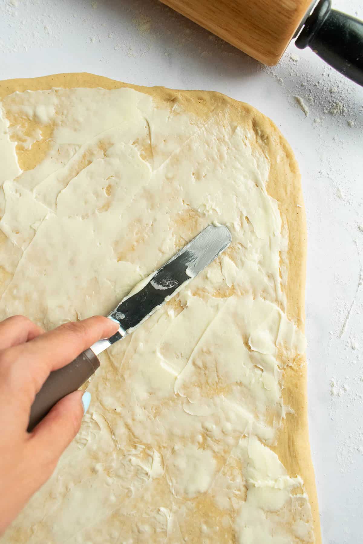 A hand spreading softened butter on dough with a small metal spatula.