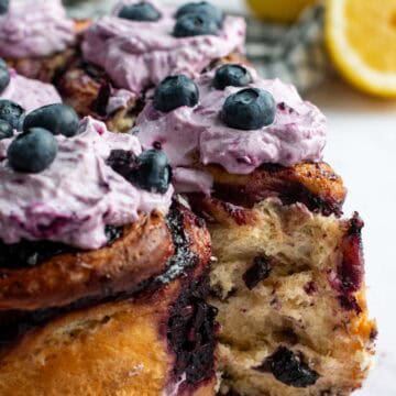 Tall cinnamon rolls topped with purple whipped creme fraiche and fresh blueberries.