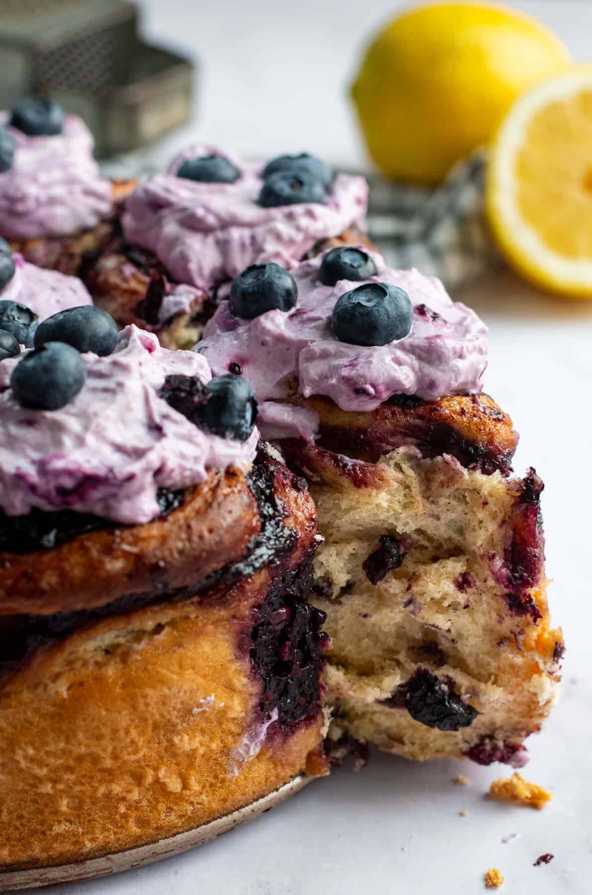 Tall cinnamon rolls topped with purple whipped creme fraiche and fresh blueberries.