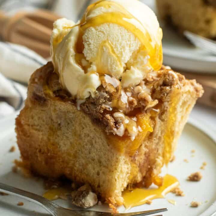 A fluffy cinnamon roll on a plate topped with streusel, vanilla ice cream, and drizzled honey.