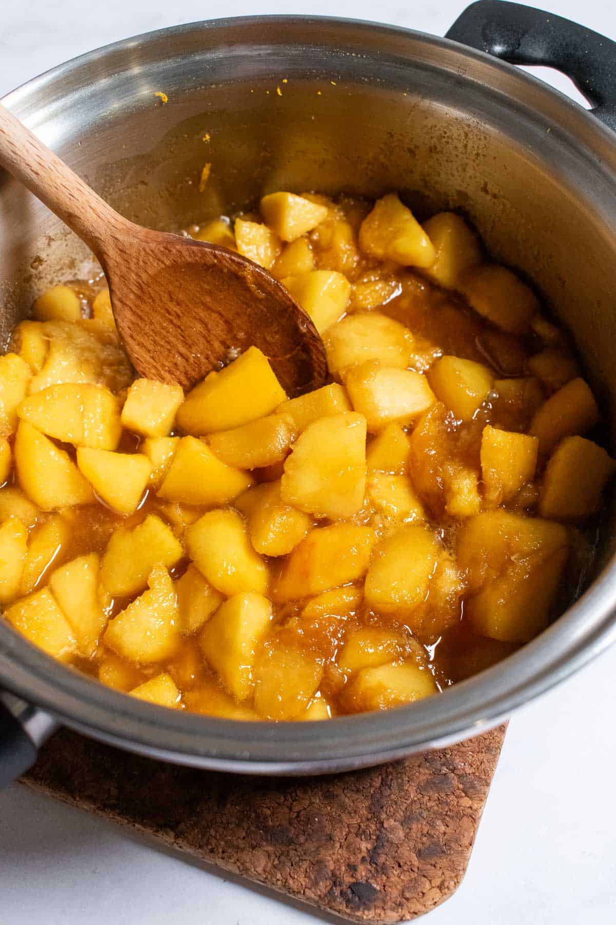 Peeled and chopped peaches in a metal saucepan with a thick sauce.