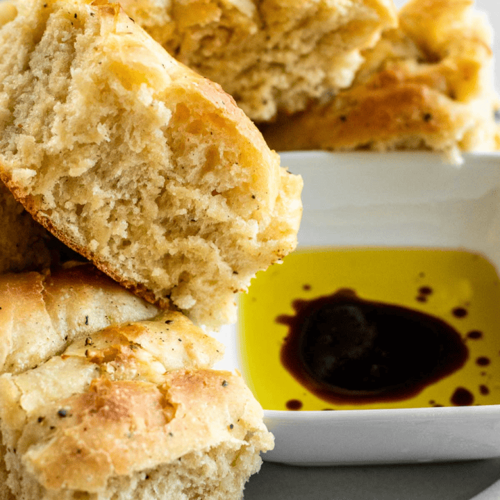 Three squares of fluffy black pepper focaccia piled around a small bowl of olive oil and balsamic vinegar.