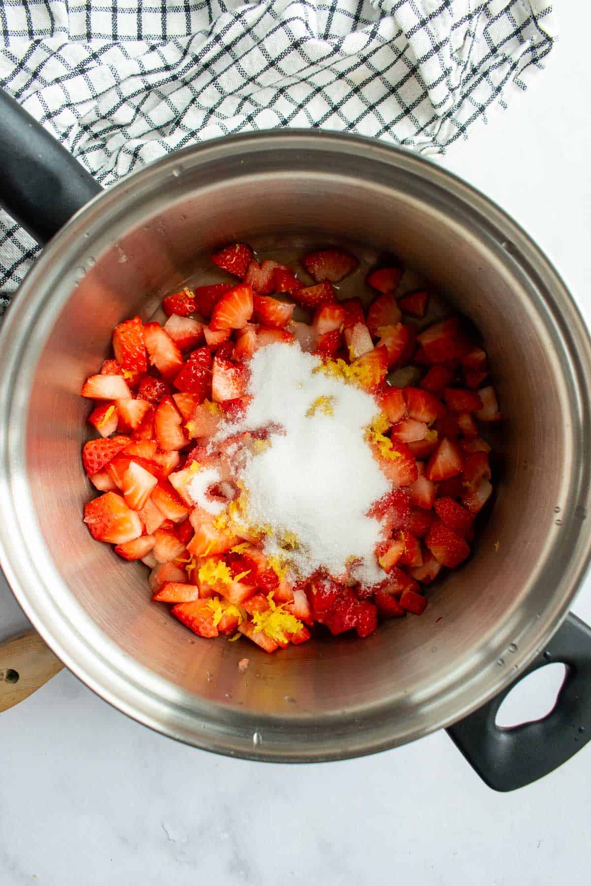 Diced strawberries, sugar, lemon zest, and lemon juice in a metal saucepan.