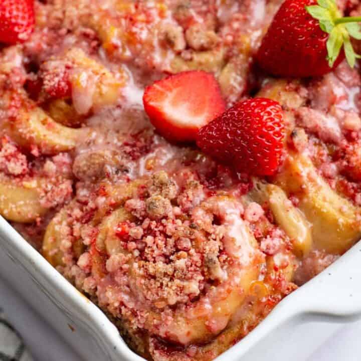Fluffy cinnamon rolls in a baking dish topped with pink crumbly streusel and fresh strawberries.