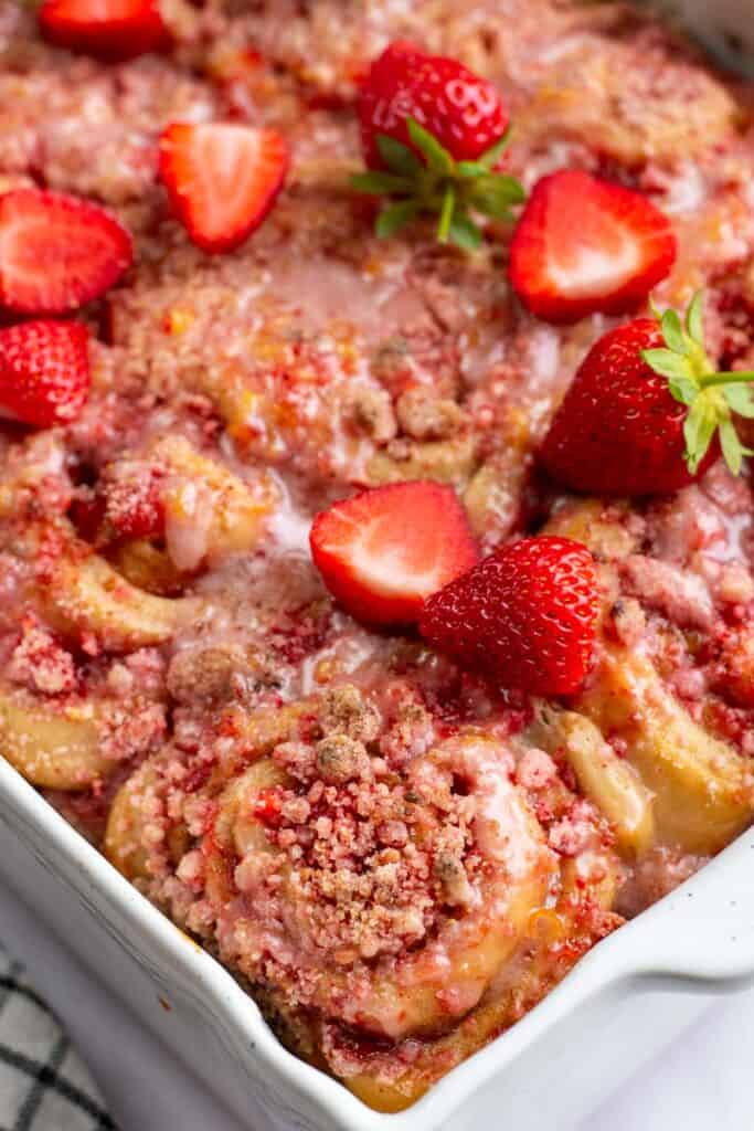Cinnamon rolls in a white baking dish topped with crumbly pink streusel and fresh strawberries.