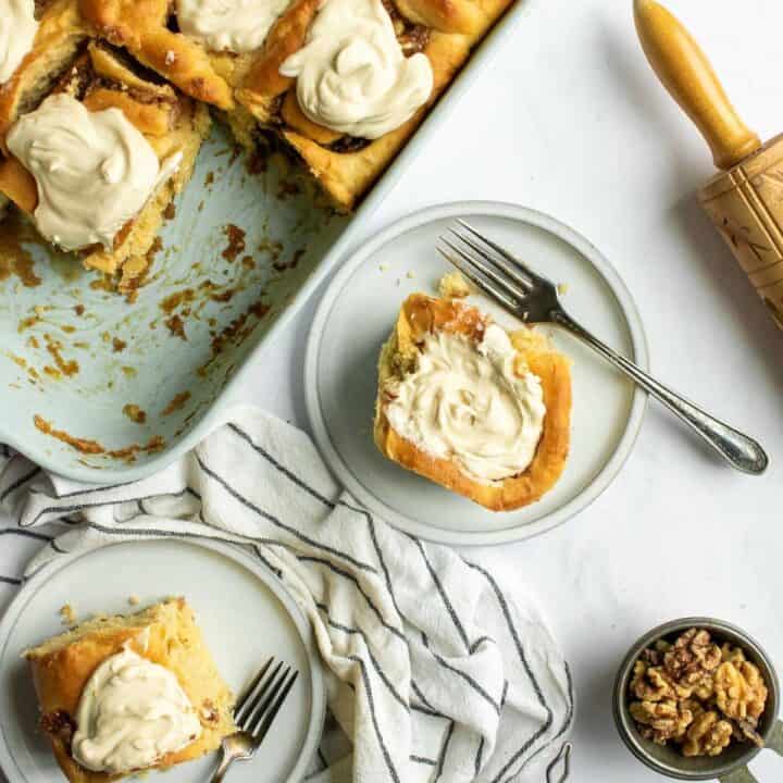 Two cinnamon rolls on grey plates topped with whipped cream.