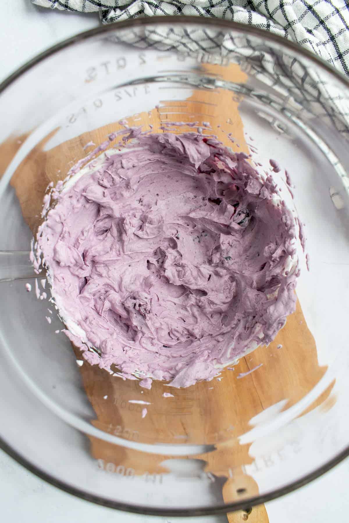 Light purple whipped creme fraiche in a glass bowl sitting on a wooden board.