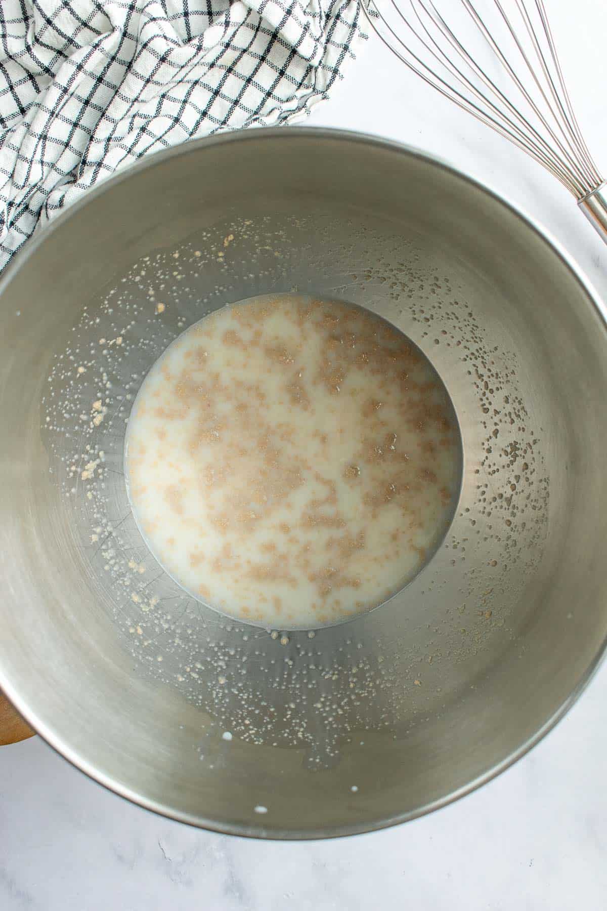 Milk, instant yeast, and sugar mixed in a large metal bowl.