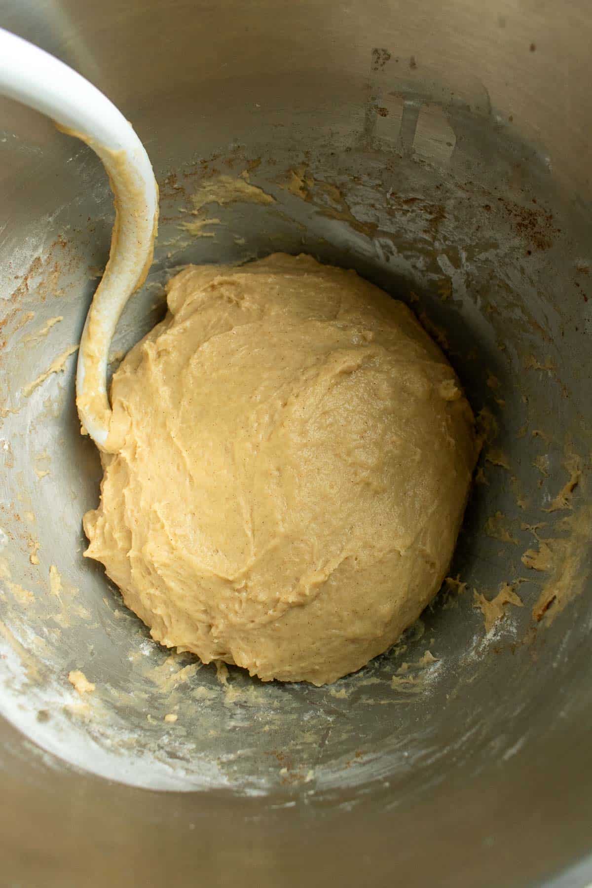 A ball of kneaded enriched bread dough in a metal bowl with a dough hook from a stand mixer.