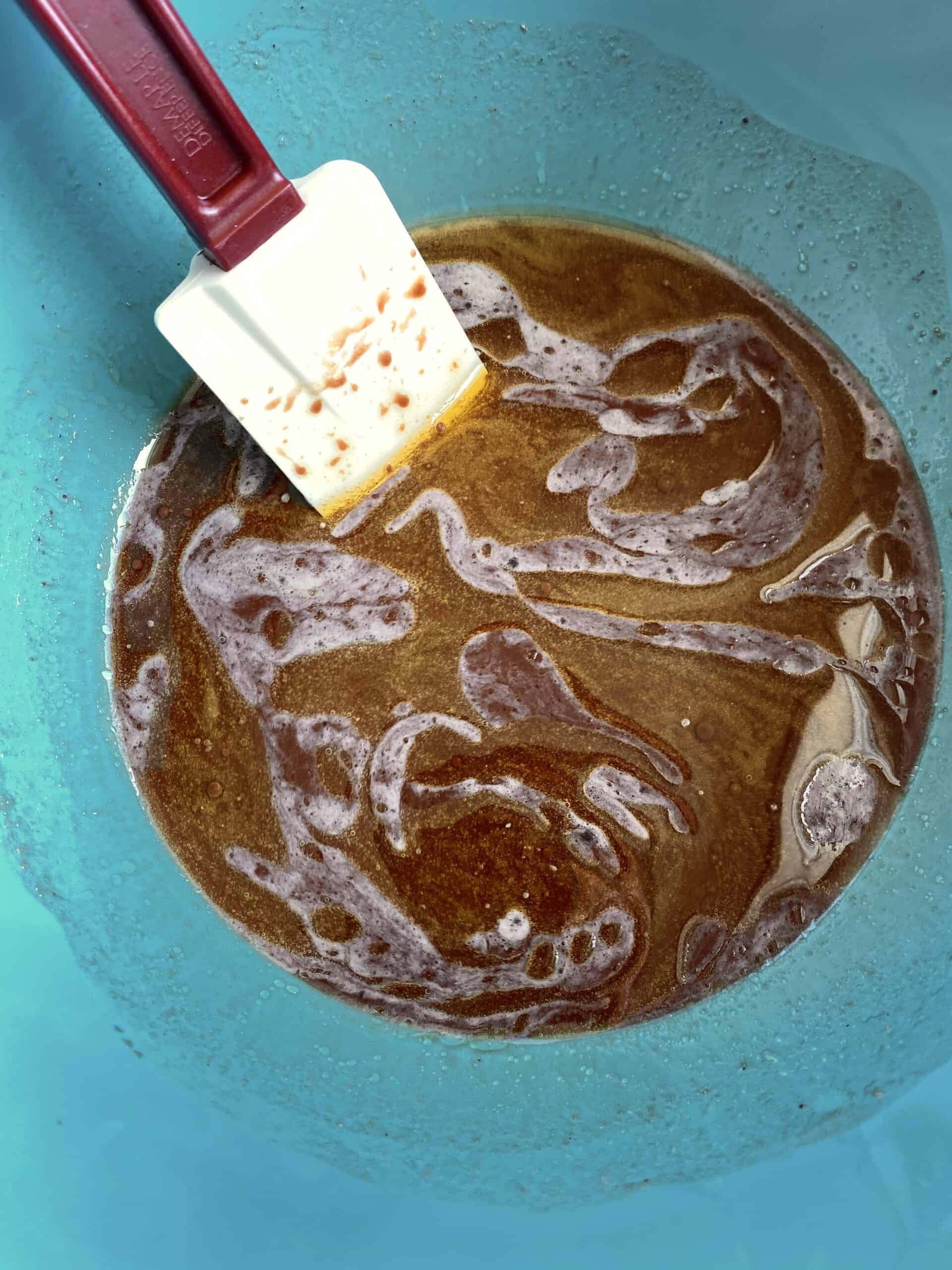 Coffee, water, olive oil, cocoa powder, yeast, and sugar mixed into a brown liquid in a blue bowl.