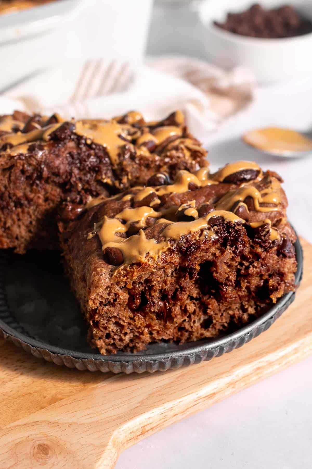 Two thick slices of chocolate focaccia drizzled with creamy peanut butter on a plate on a wood board. 