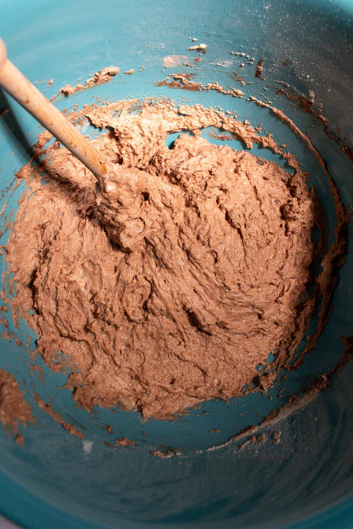 A wet, sticky chocolate bread dough in a blue bowl with a wooden spoon.