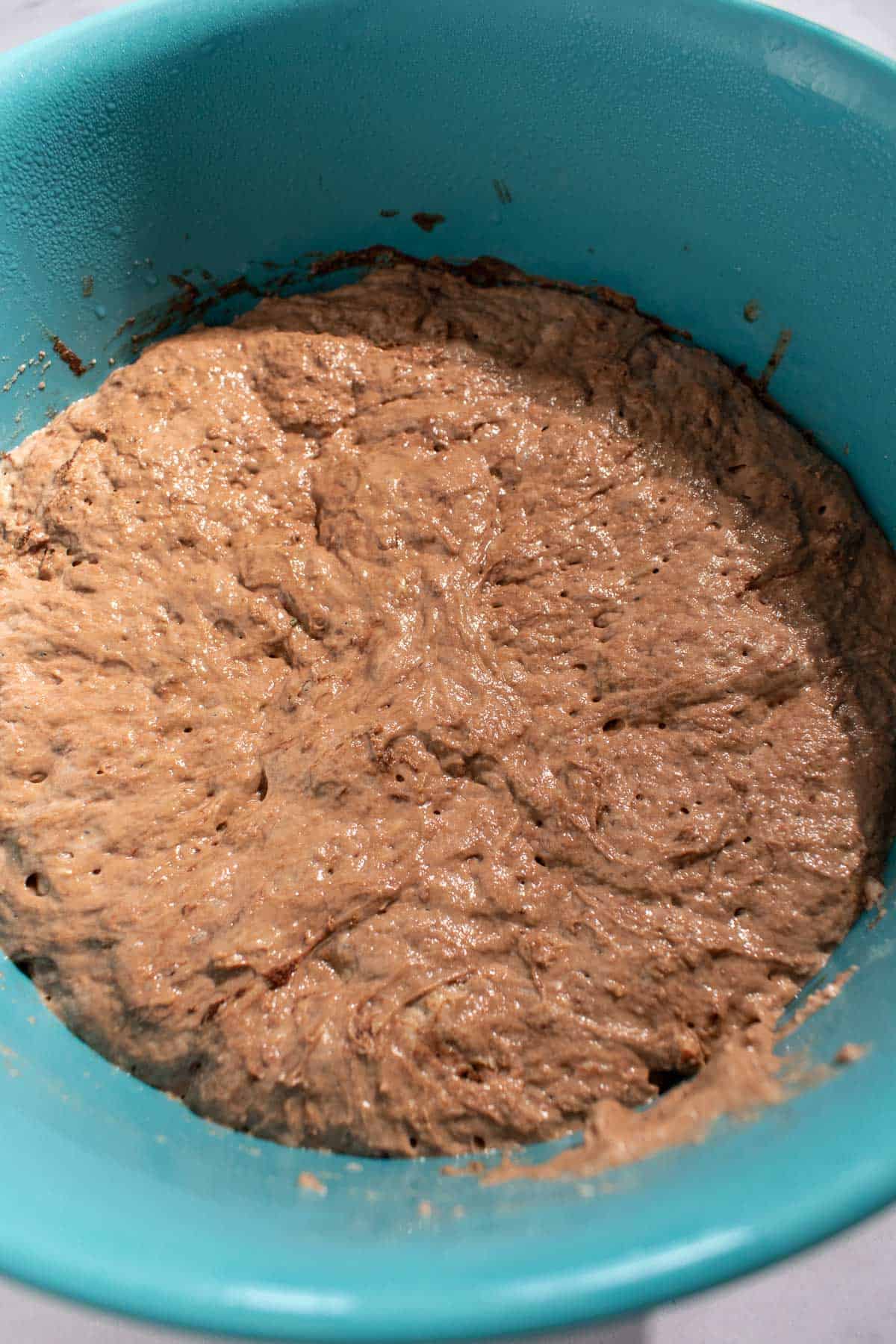 Risen, bubbly chocolate focaccia dough in a large blue mixing bowl.