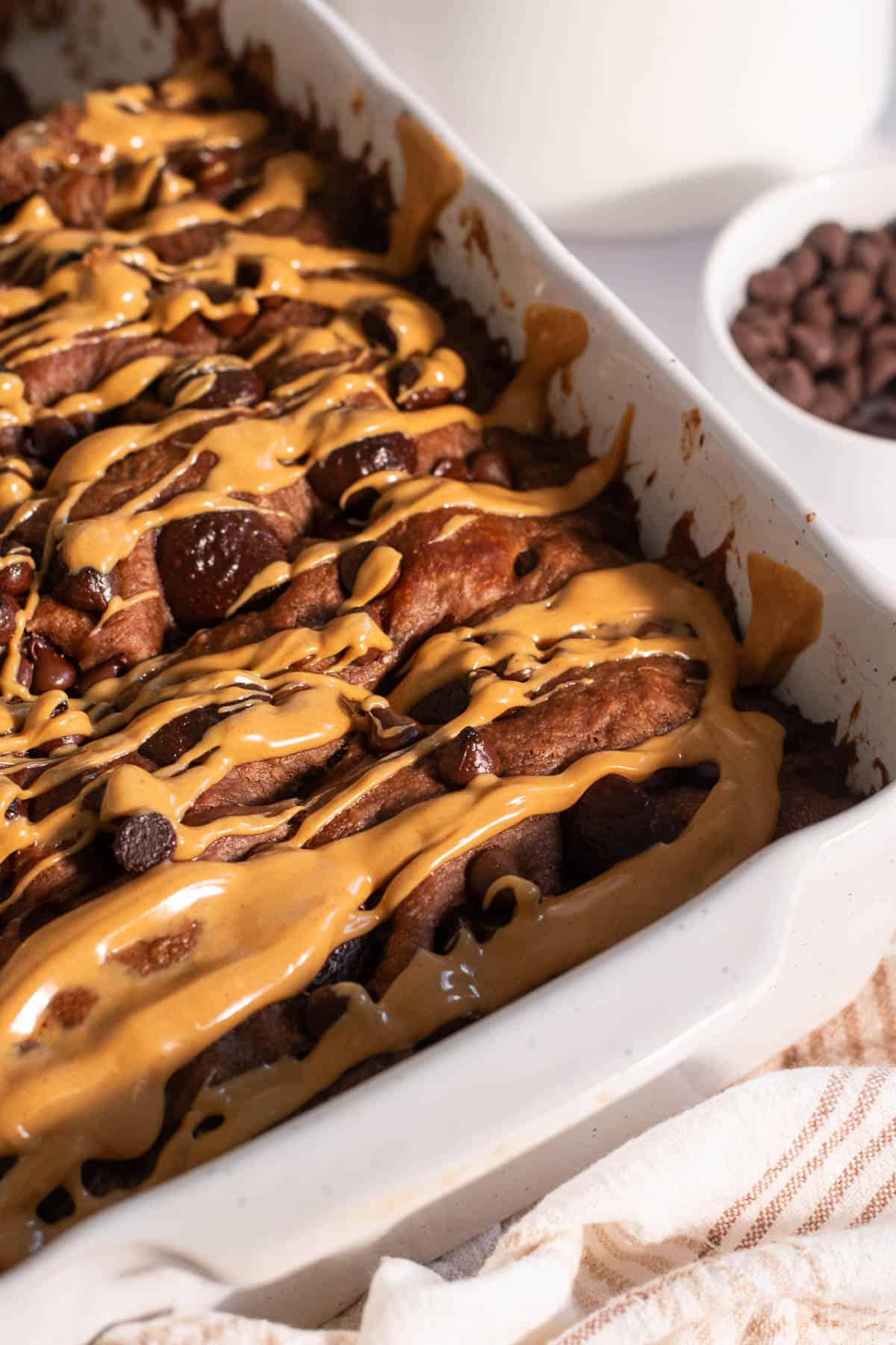 A loaf of chocolate peanut butter focaccia in a white baking dish with peanut butter drizzled on top.