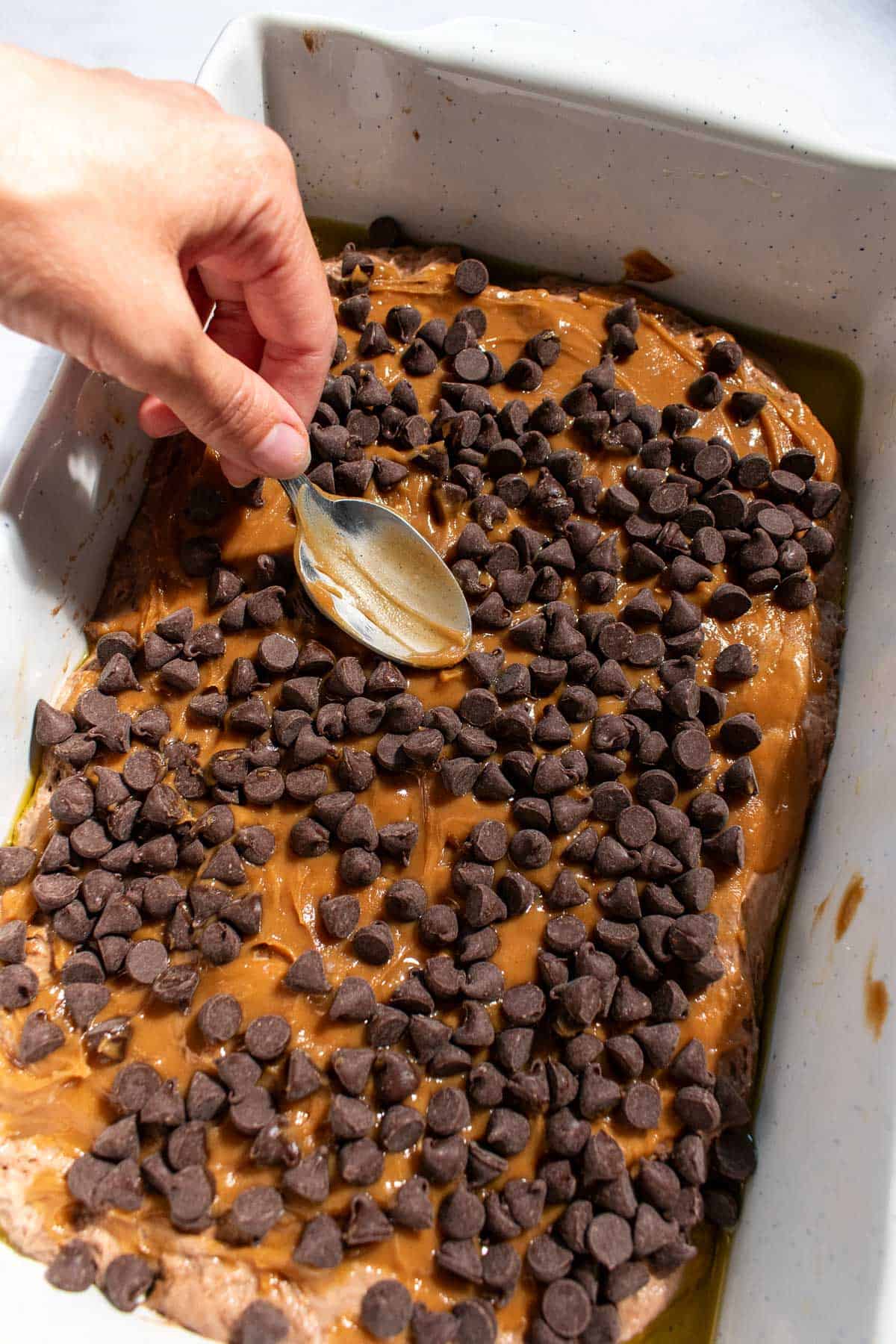A hand spreading peanut butter onto chocolate focaccia dough with the back of a spoon.