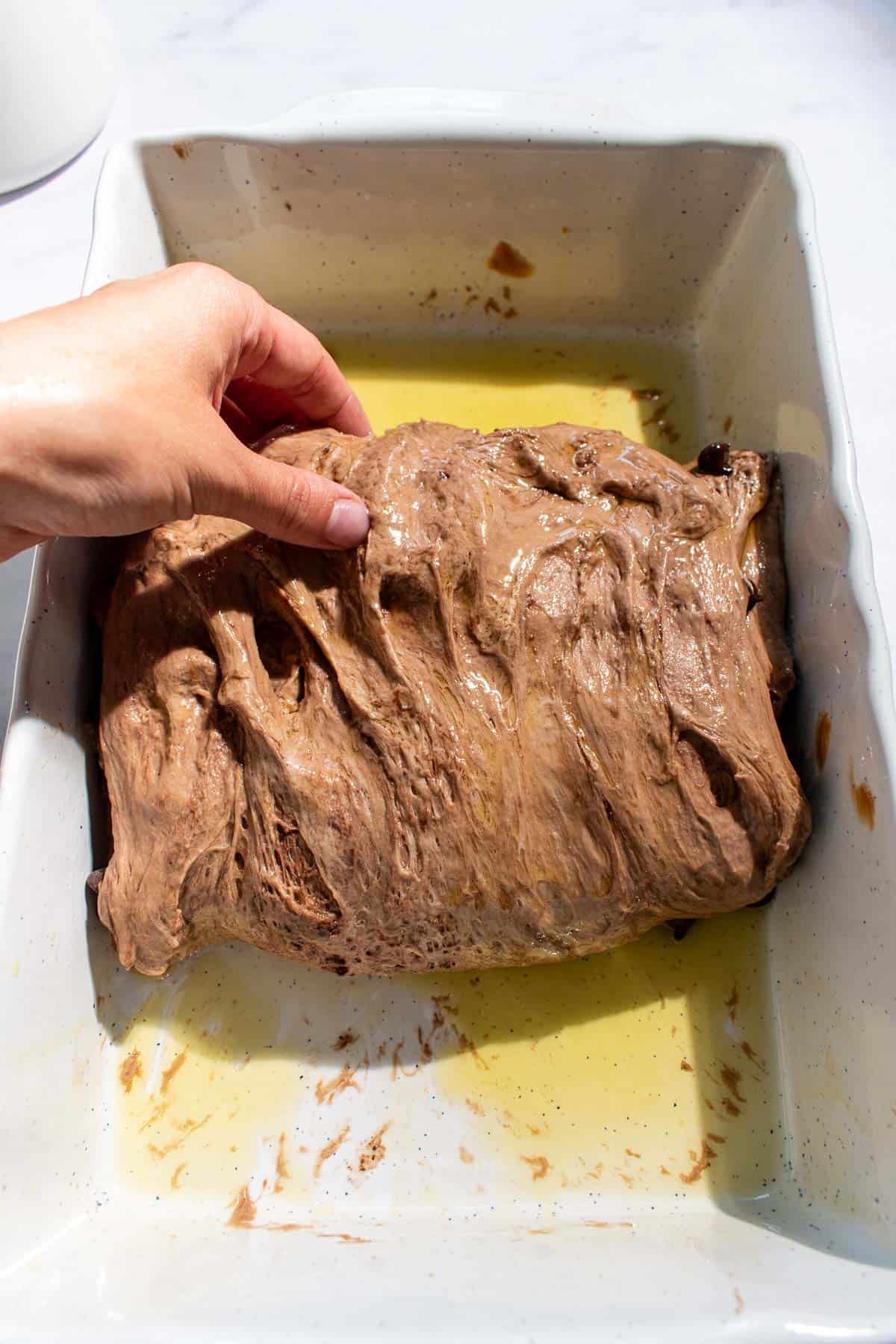 A hand folding chocolate bread dough with a letter fold in a baking dish greased with olive oil.