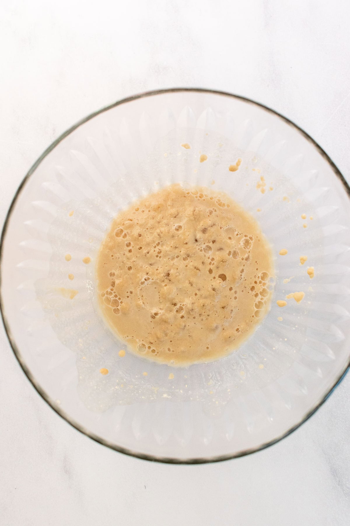 Frothy, activated yeast in water in a small glass bowl.