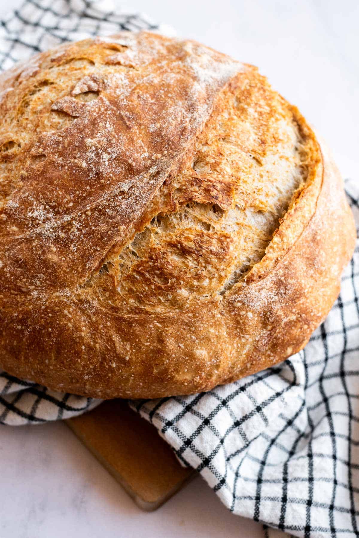 A golden, crusty loaf of country bread on a white and black checkered linen.