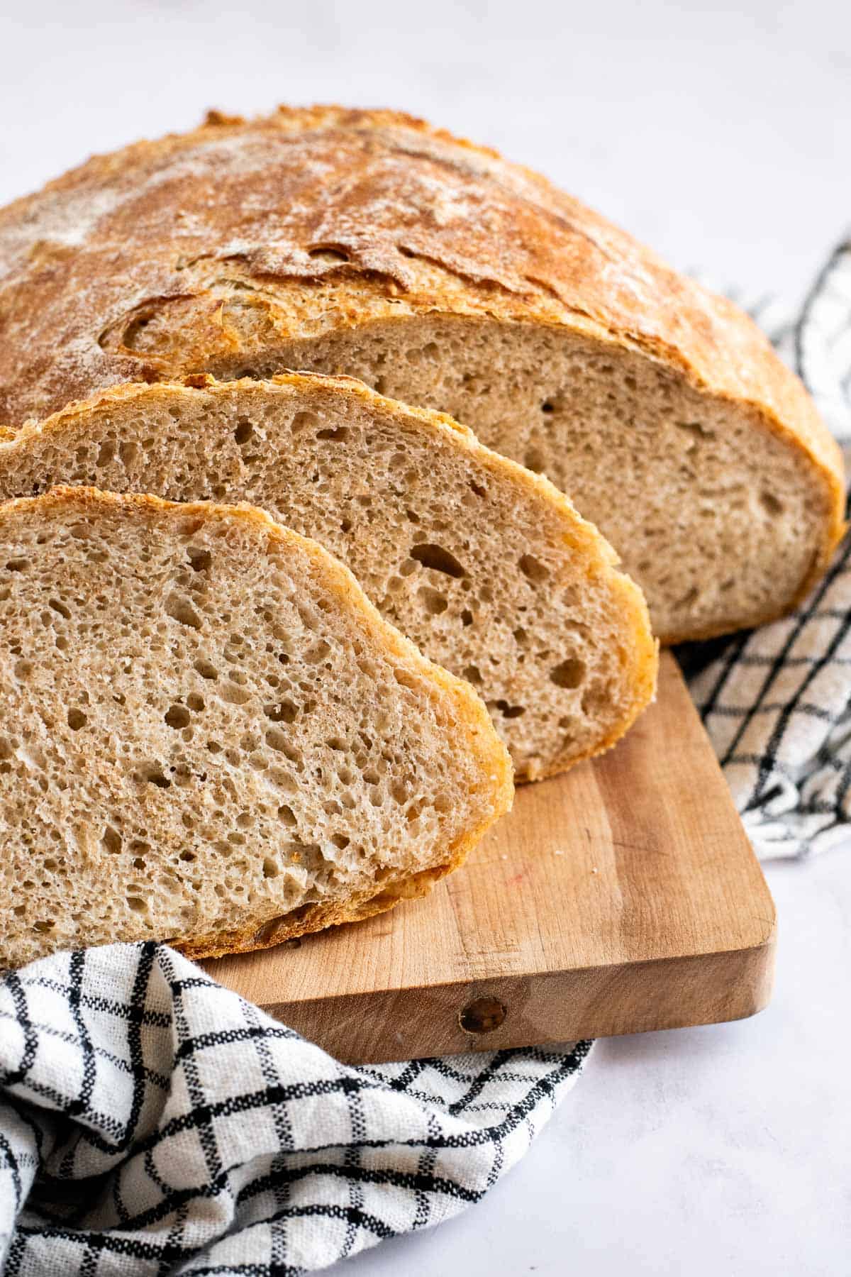 Two slices of airy country bread on a cutting board leaning against the rest of the loaf.