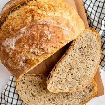 Two slices of country bread next to the rest of the crusty loaf on a wooden board.