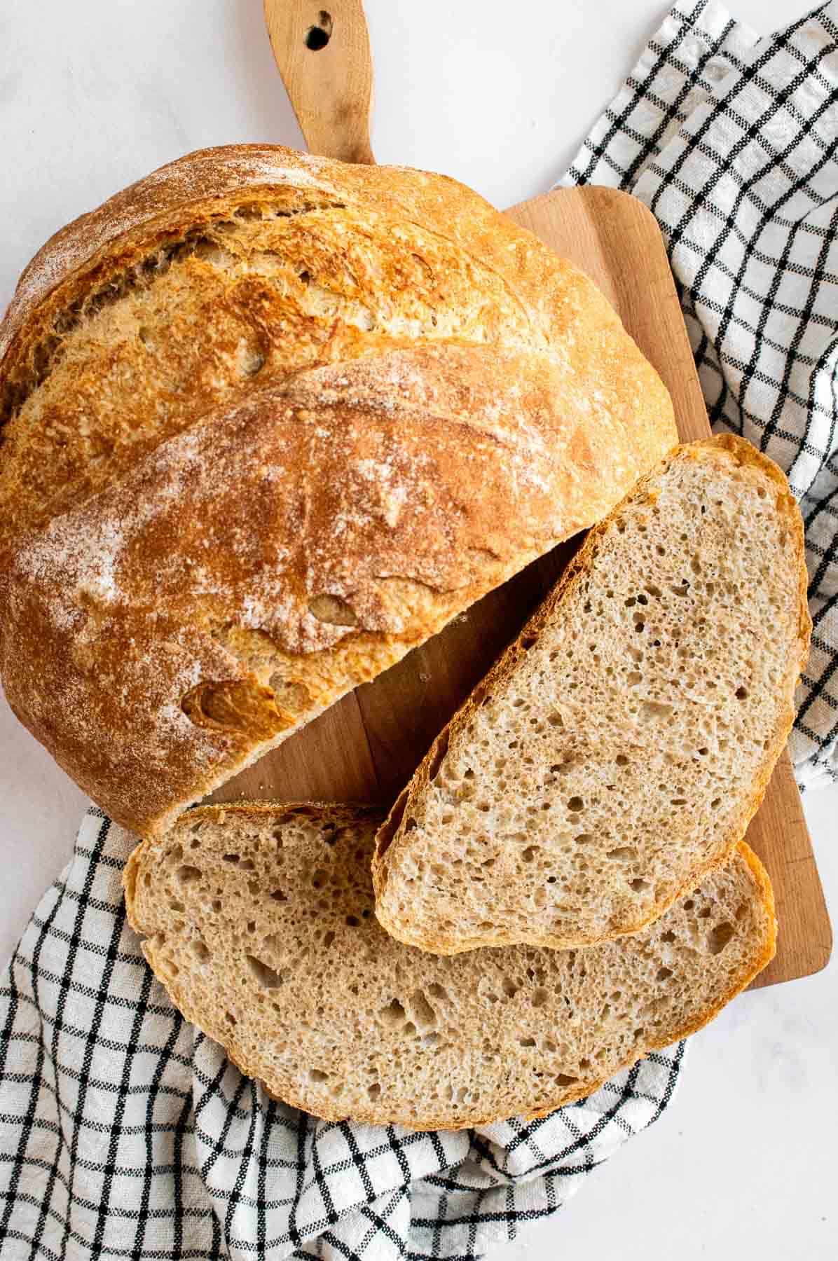 Two slices of country bread next to the rest of the crusty loaf on a wooden board.