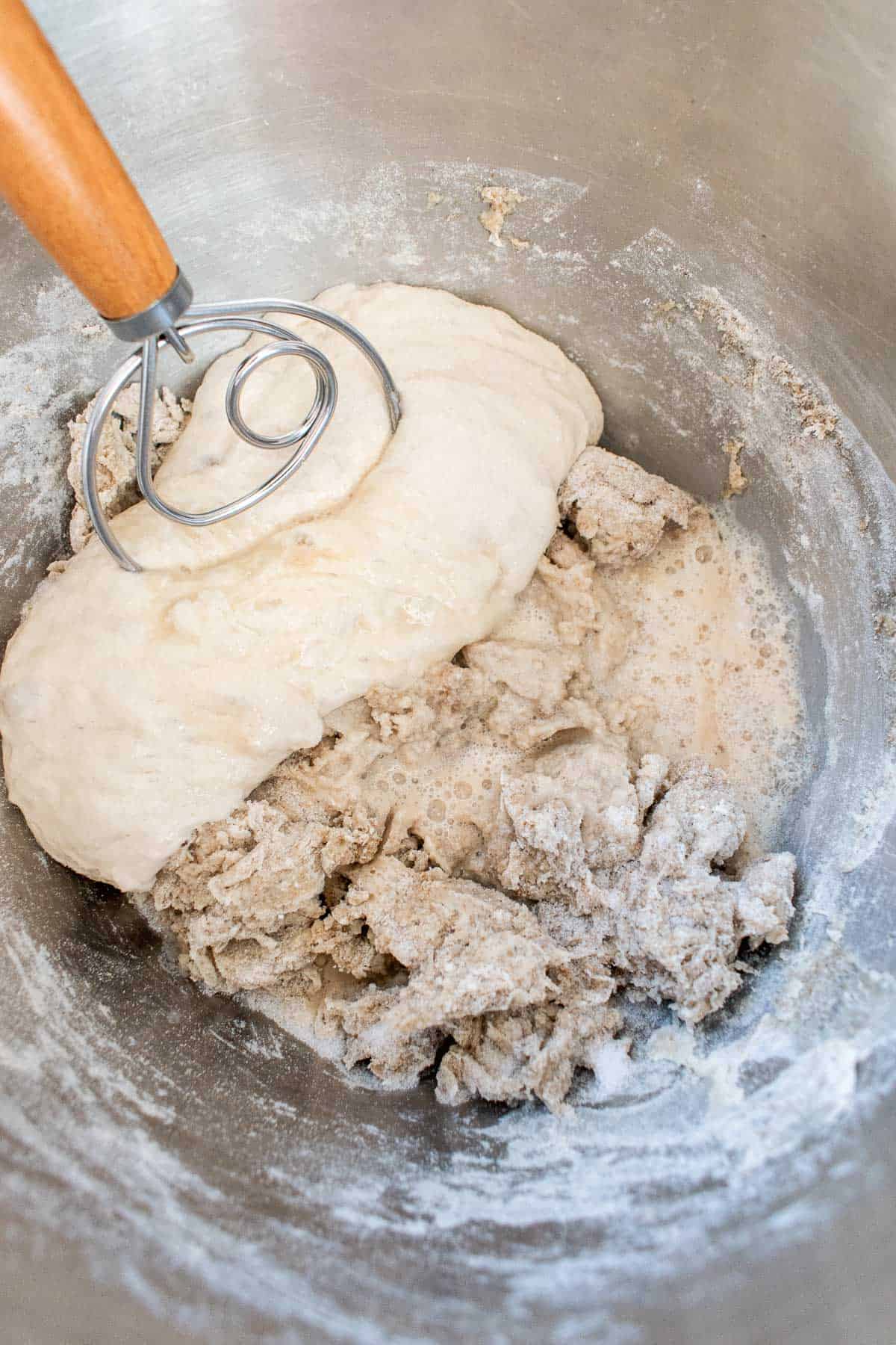 A Danish dough whisk in a mixing bowl with a shaggy dough, yeast dissolved in water, and wet, sticky poolish.