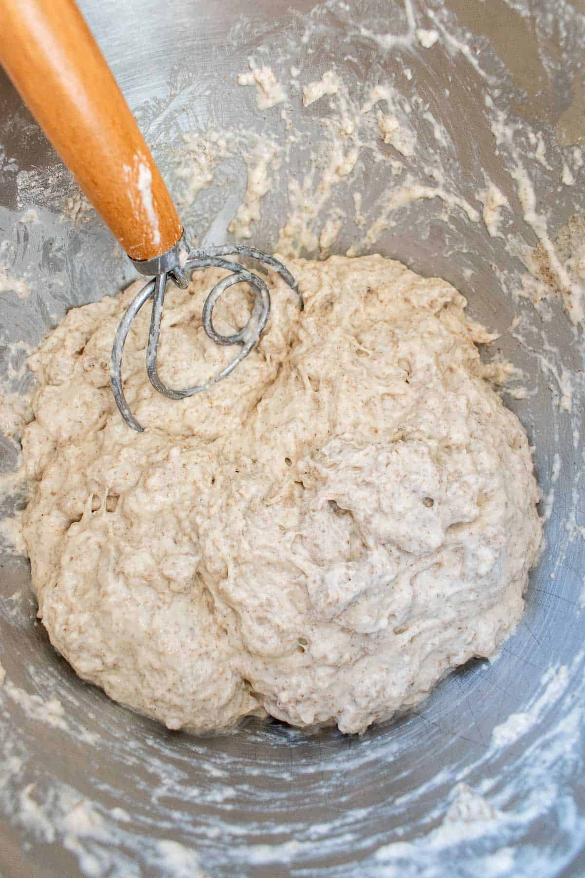 A rough, wet dough in a metal mixing bowl with a Danish dough whisk.