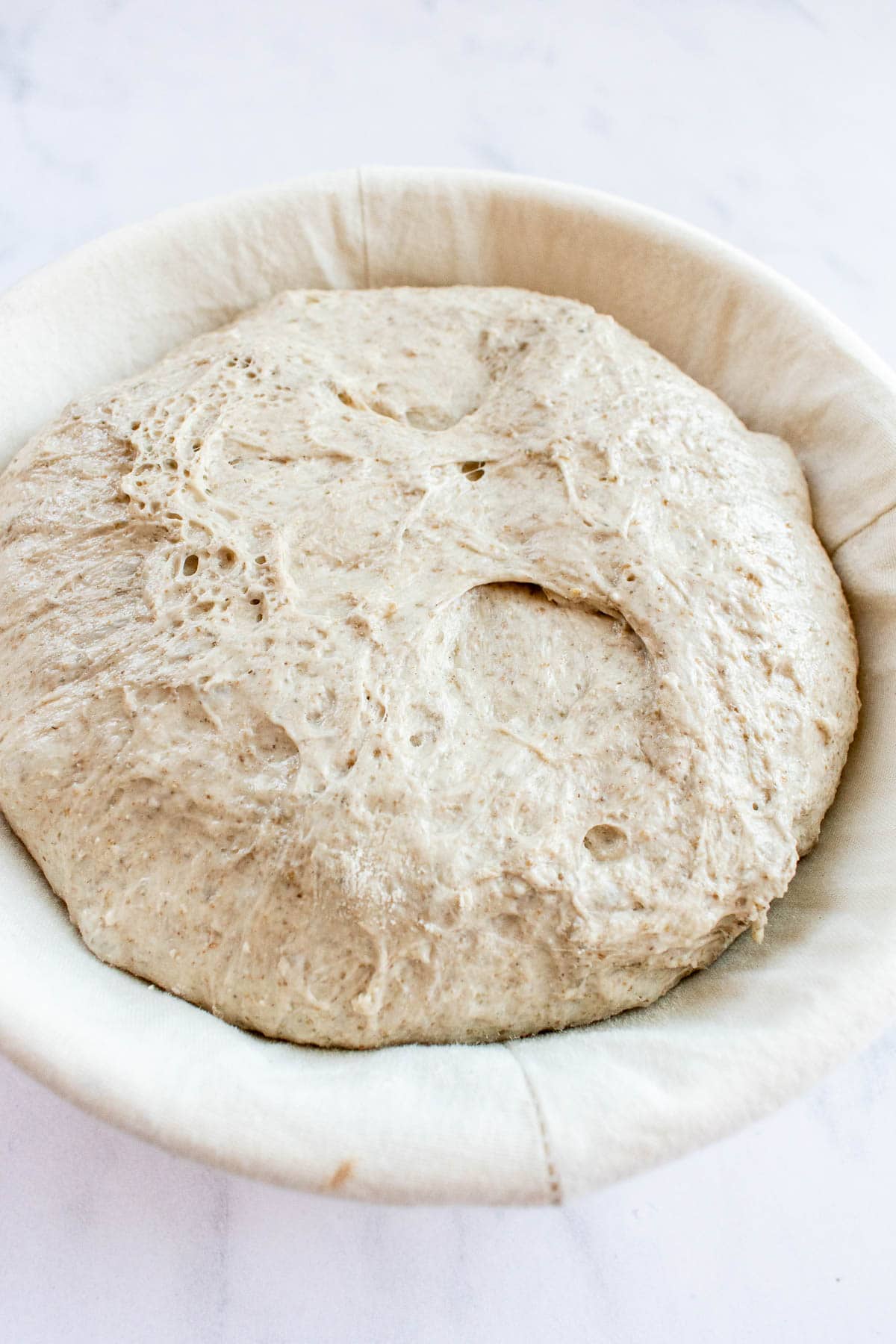 A proofed boule of country bread dough in a proofing basket lined with cloth.
