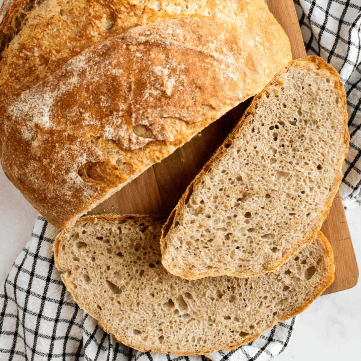 Two slices of rustic country bread on a wooden board on top of a kitchen linen.