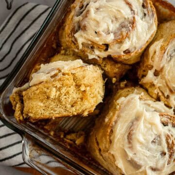 Four cinnamon rolls in a glass dish topped with white frosting, with one cinnamon roll on its side.