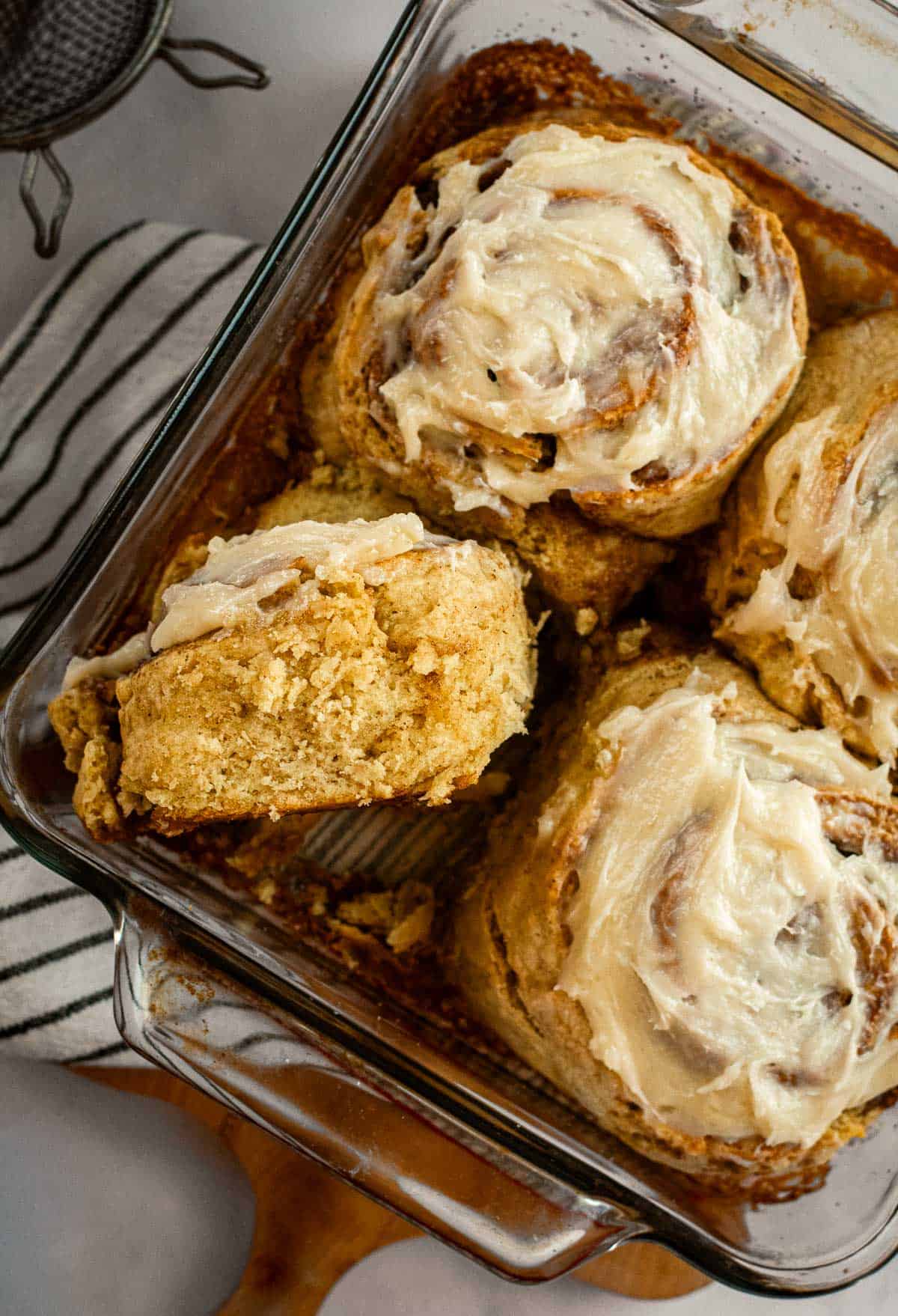 Four cinnamon rolls in  a glass dish topped with white frosting, with one cinnamon roll on its side.