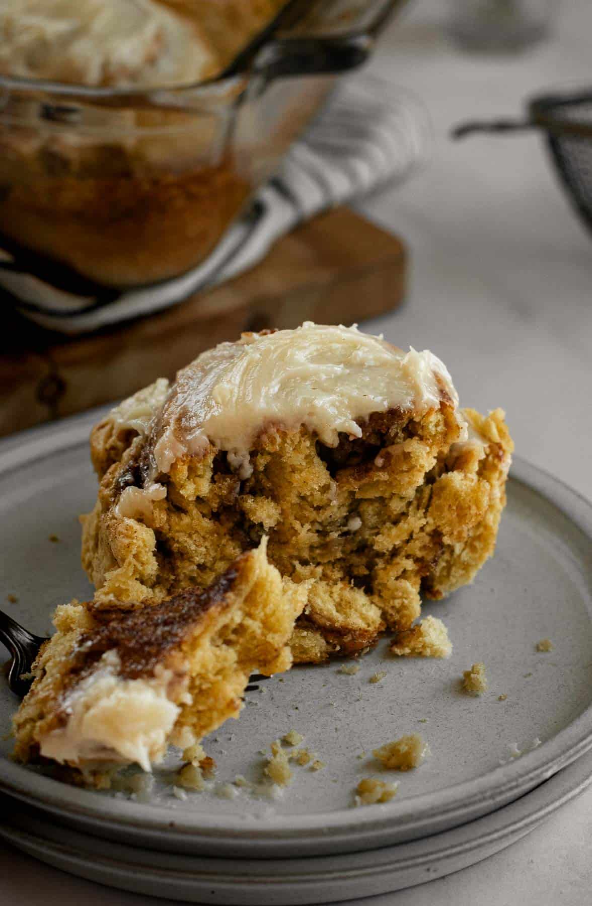 A half-eaten cinnamon roll topped with creamy frosting on a grey plate.