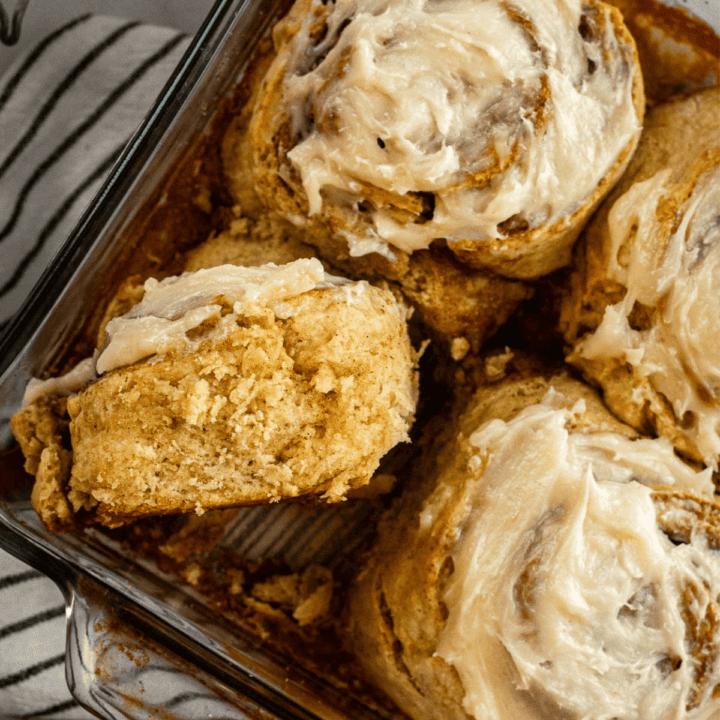 Four large cinnamon rolls topped with frosting in a square baking dish.