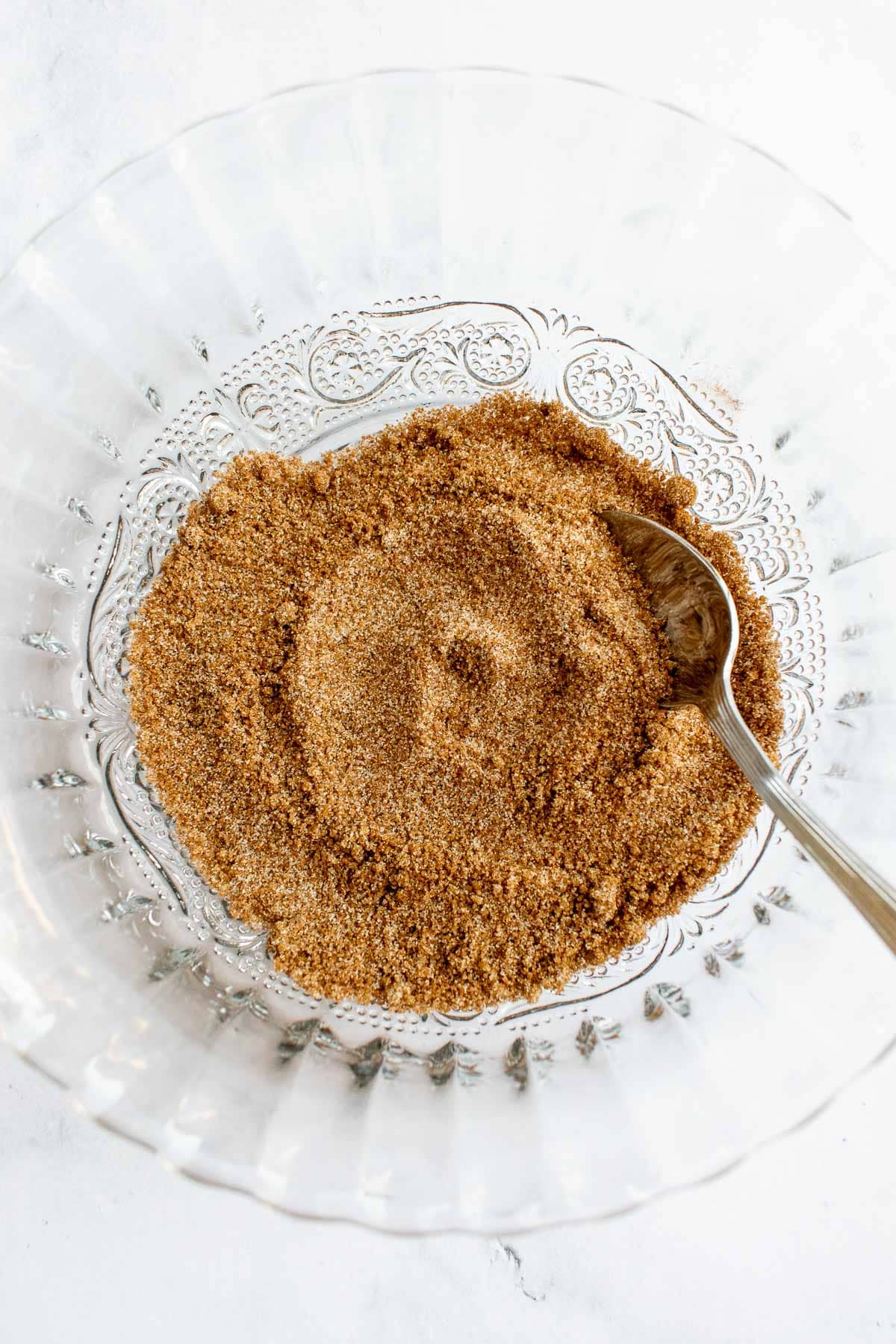 A bowl of brown sugar, white sugar, and cinnamon mixed together with a spoon resting inside.