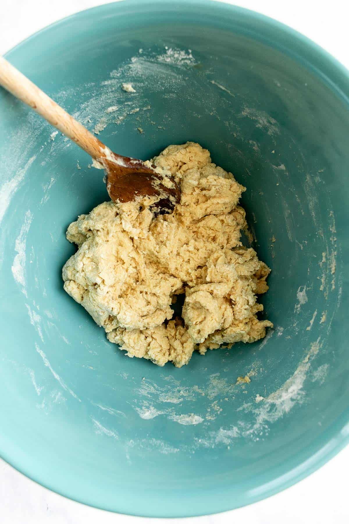 A shaggy bread dough in a blue mixing bowl with a large wooden spoon.
