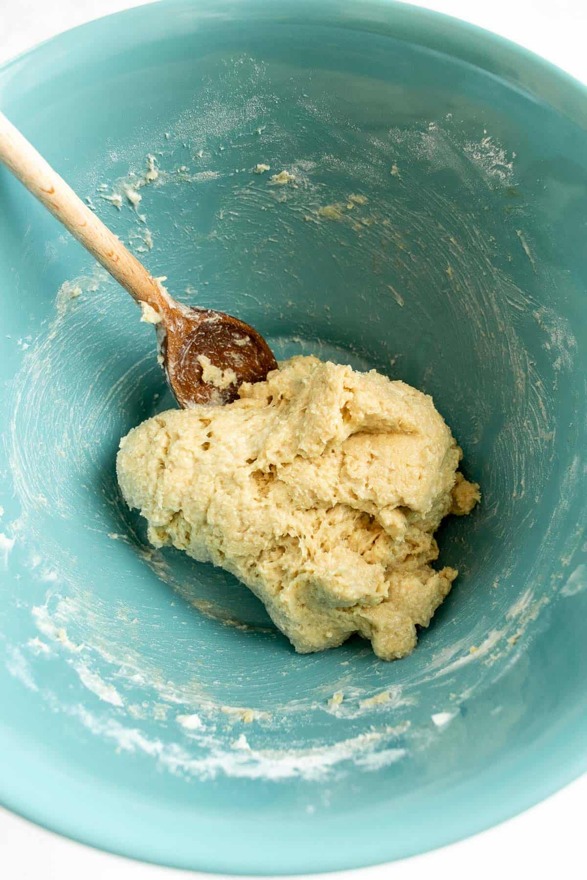 An enriched dough mixed into a rough ball in a blue bowl with a large wooden spoon.